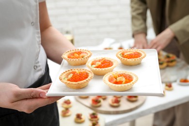 Photo of Woman holding board with tasty canapes indoors, closeup