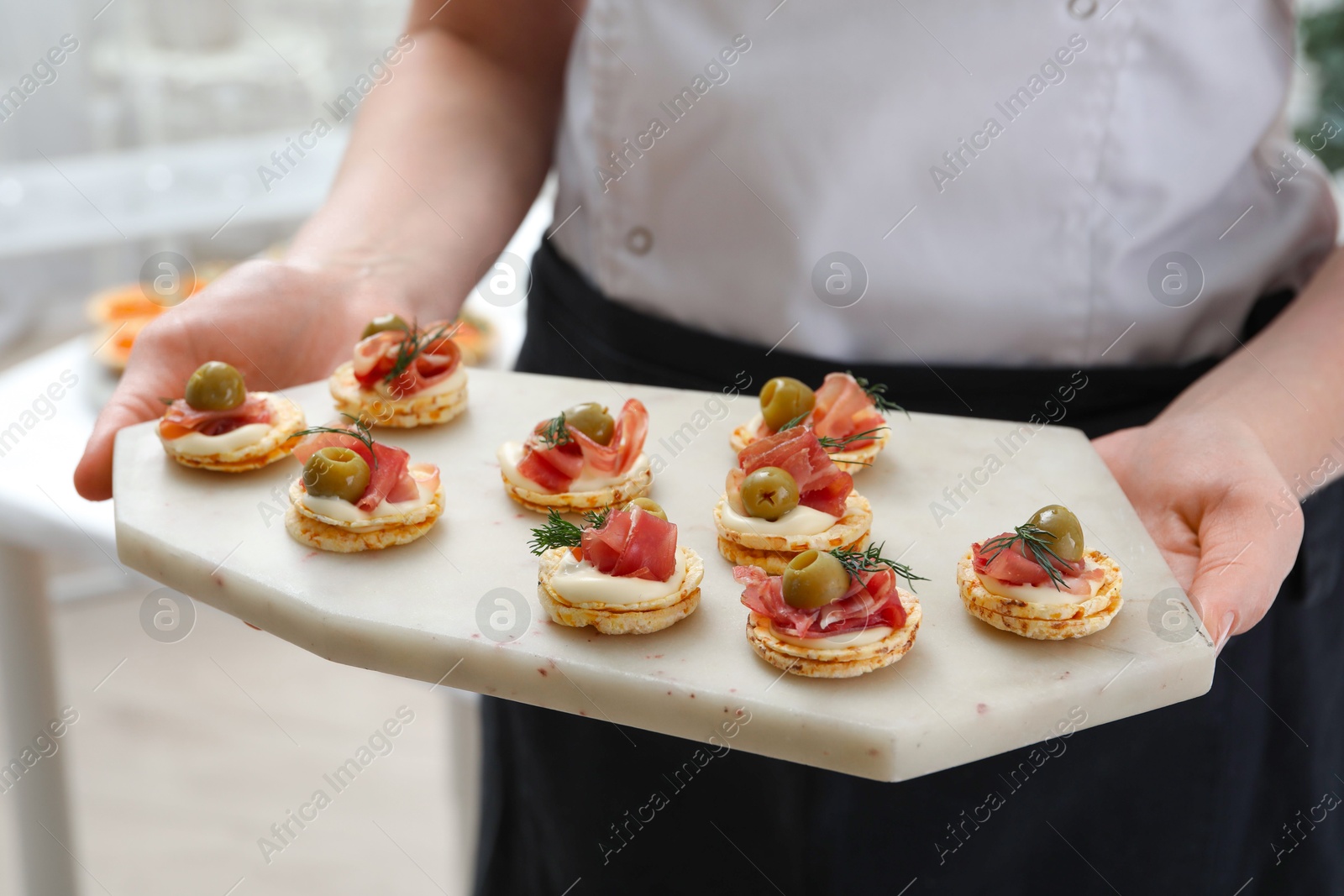 Photo of Woman holding board with tasty canapes indoors, closeup