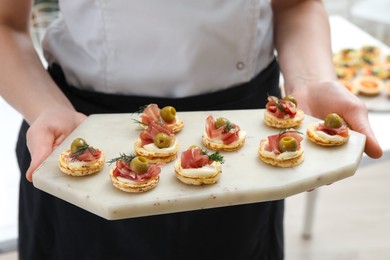 Photo of Woman holding board with tasty canapes indoors, closeup