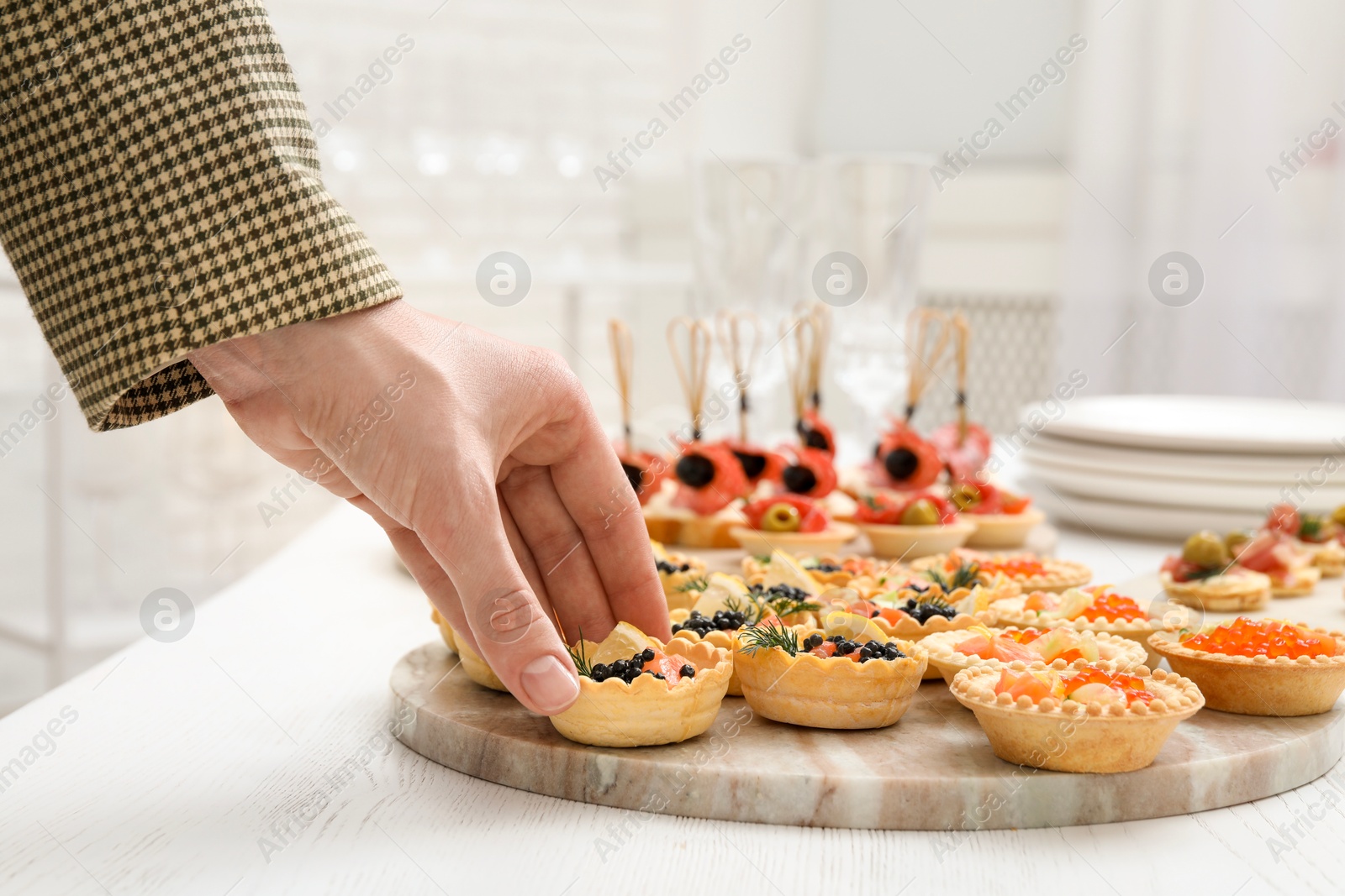 Photo of Woman taking tasty canape at white wooden table, closeup