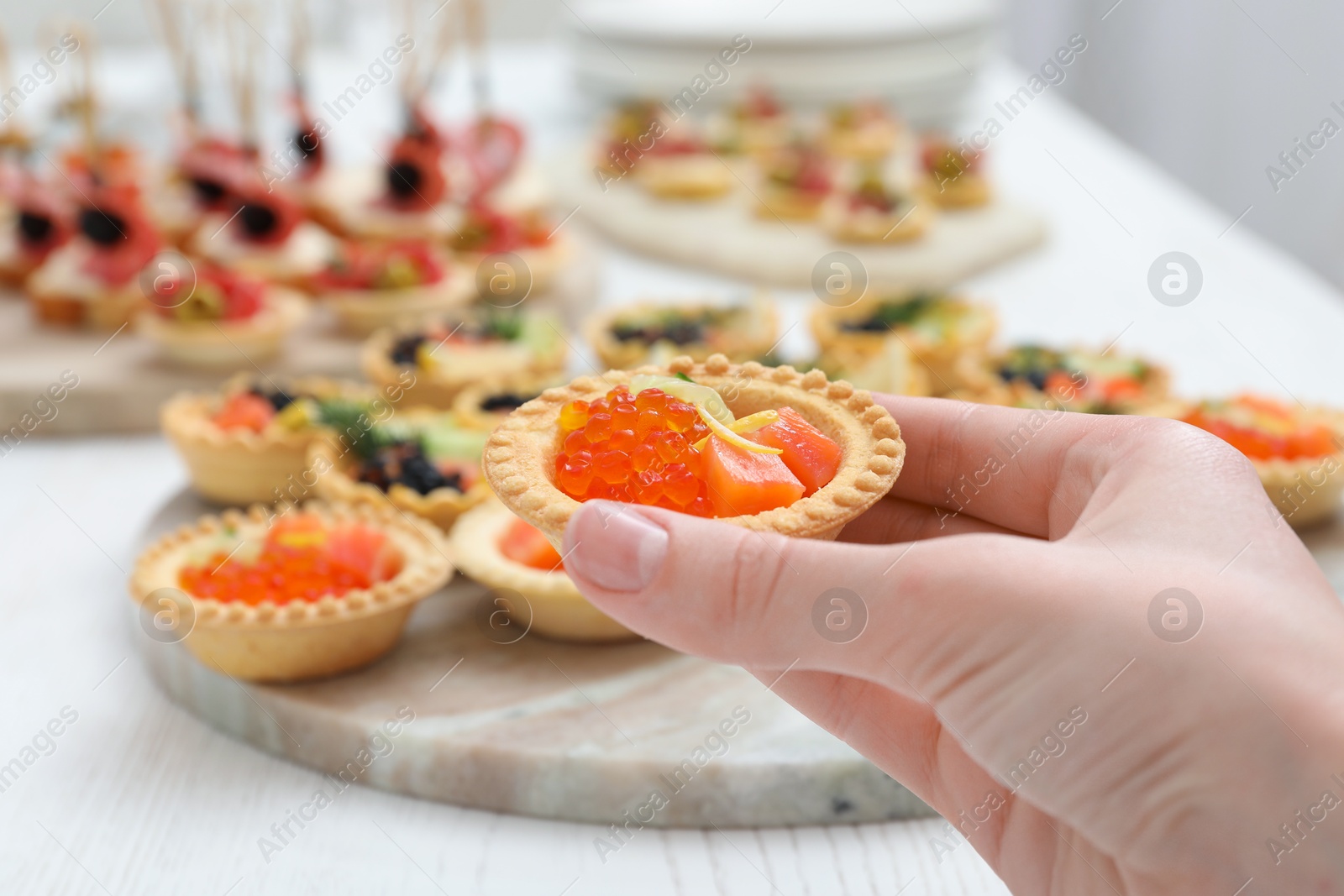 Photo of Woman taking tasty canape at white wooden table, closeup