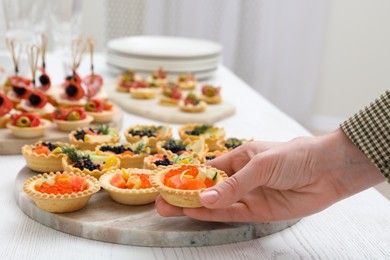 Photo of Woman taking tasty canape at white wooden table, closeup