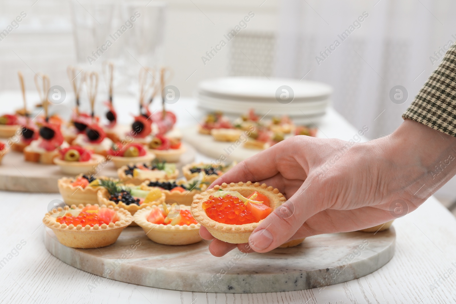 Photo of Woman taking tasty canape at white wooden table, closeup