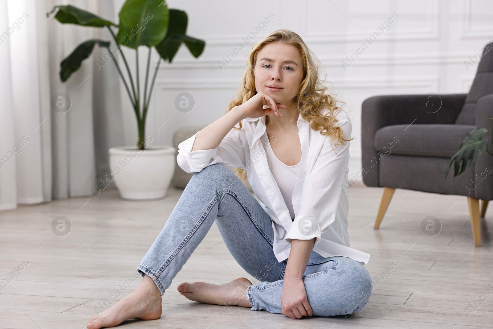 Photo of Beautiful young woman in stylish jeans sitting on floor at home