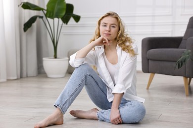 Beautiful young woman in stylish jeans sitting on floor at home