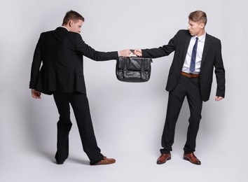 Photo of Competition concept. Businessmen pulling leather briefcase on grey background