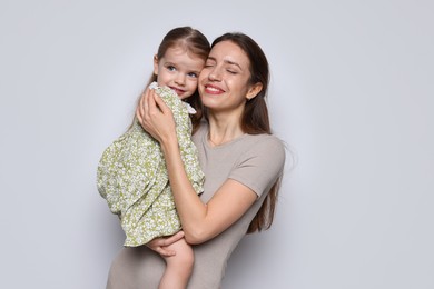 Happy mother with her cute little daughter on grey background