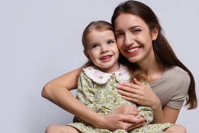 Portrait of happy mother with her cute little daughter on grey background