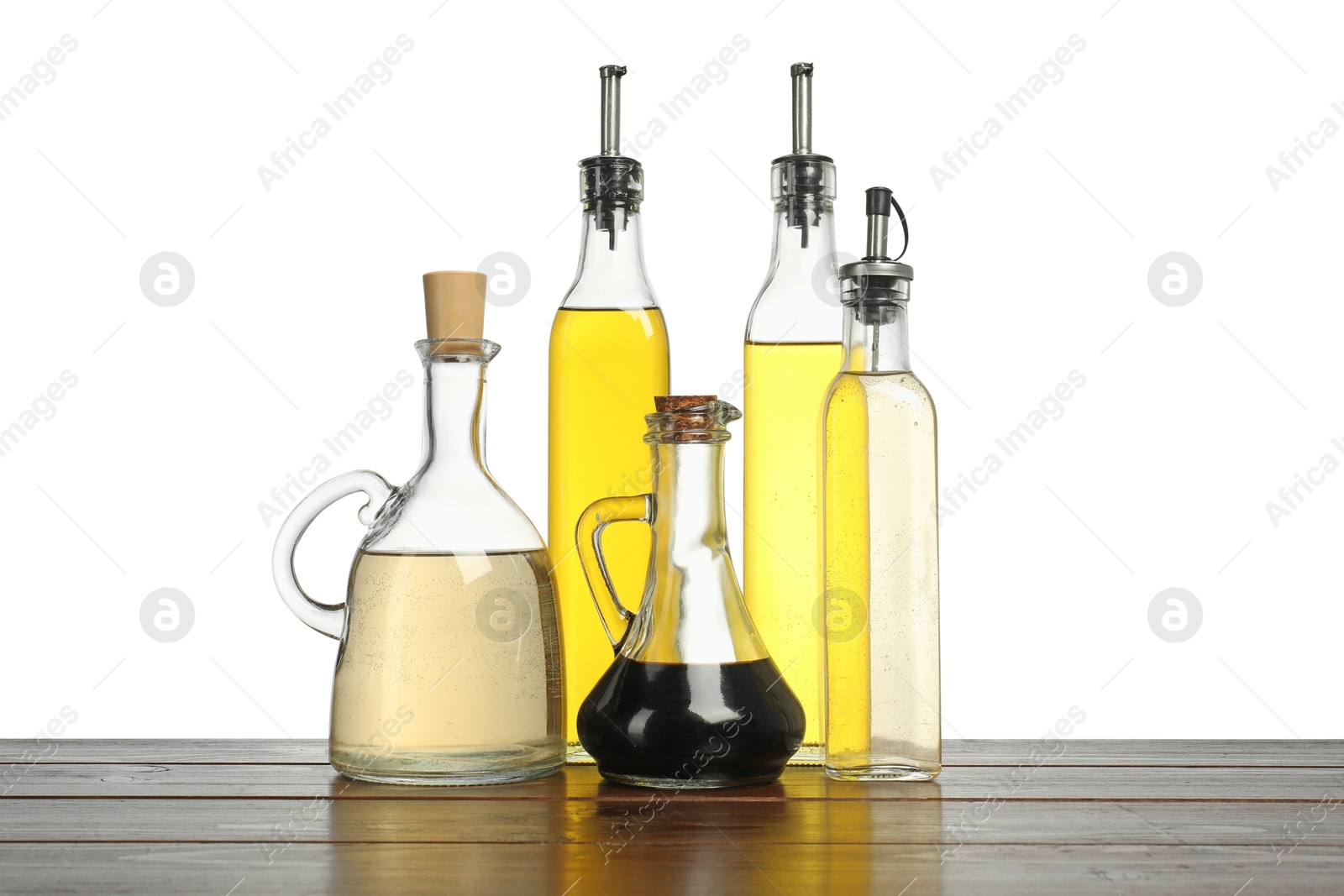 Photo of Oils and vinegars in bottles on wooden table against white background