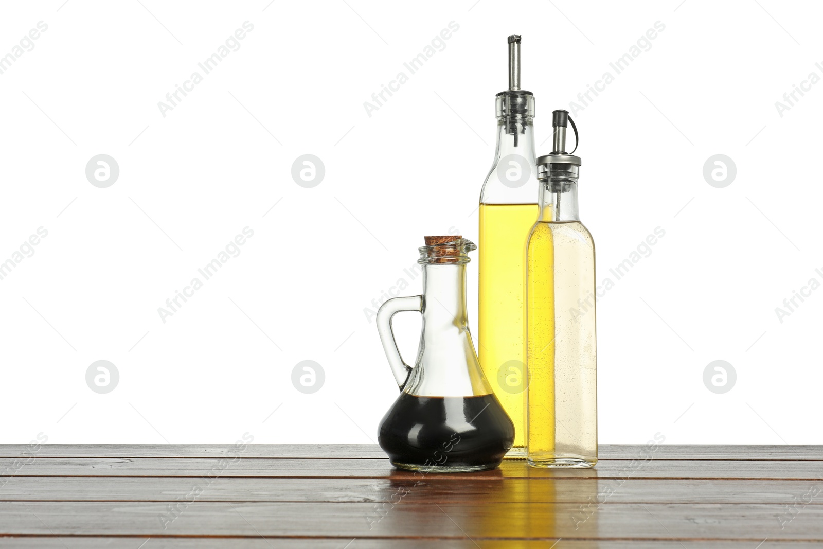 Photo of Oil and vinegars in bottles on wooden table against white background