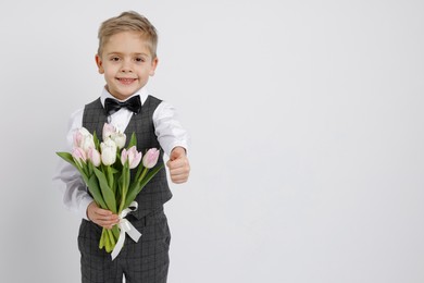 Photo of Cute little boy with bouquet of tulips showing thumbs up on white background. Space for text