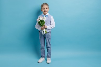 Cute little boy with bouquet of tulips on light blue background