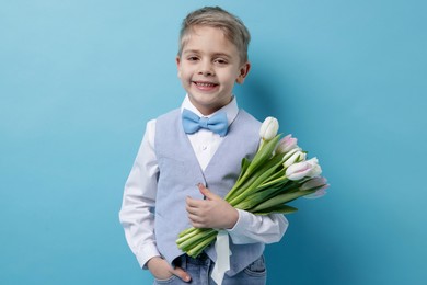 Cute little boy with bouquet of tulips on light blue background