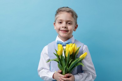 Photo of Cute little boy with bouquet of tulips on light blue background