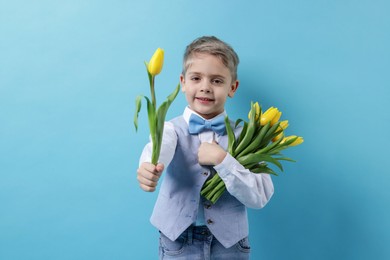 Photo of Cute little boy with bouquet of tulips on light blue background