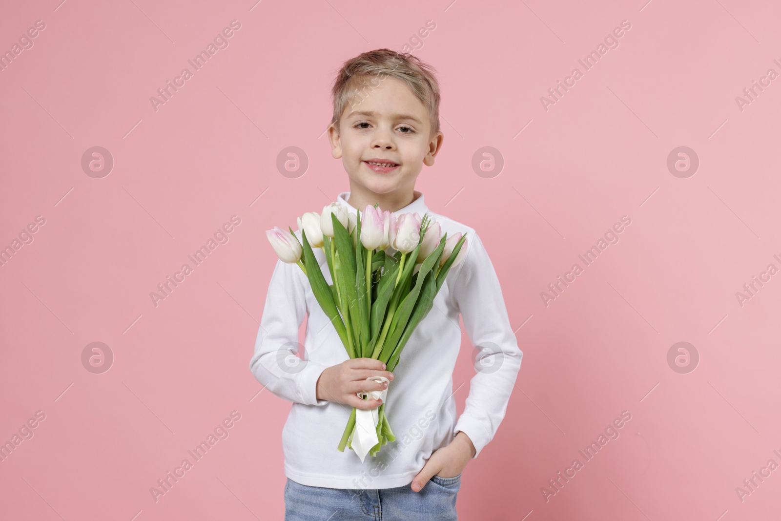 Photo of Cute little boy with bouquet of tulips on light pink background