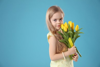 Cute little girl with beautiful yellow tulips on light blue background, space for text. Spring season