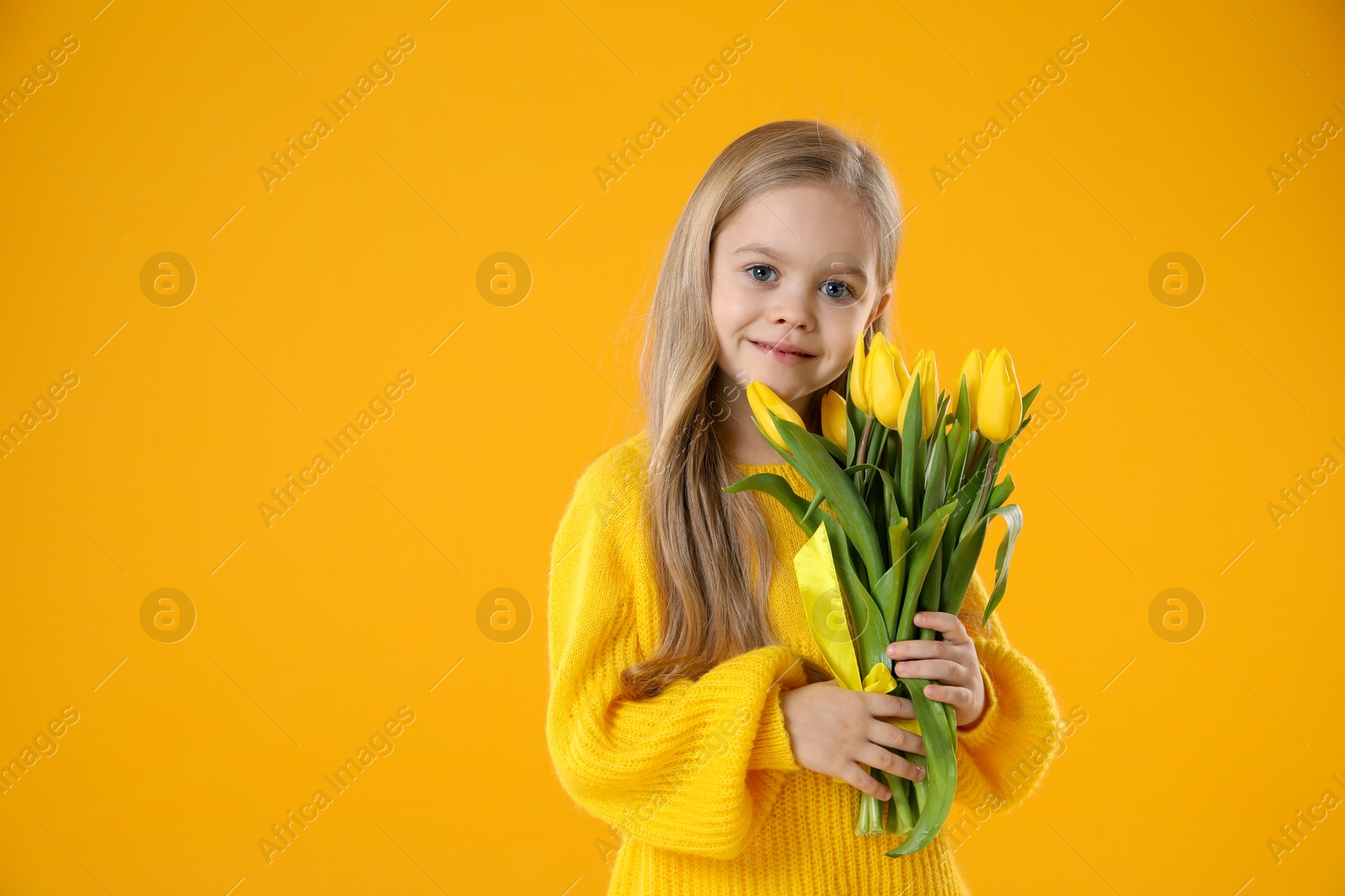 Photo of Cute little girl with beautiful yellow tulips on orange background, space for text. Spring season