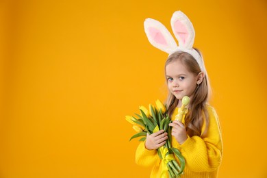 Cute little girl with bunny ears and tulips on orange background, space for text. Easter celebration