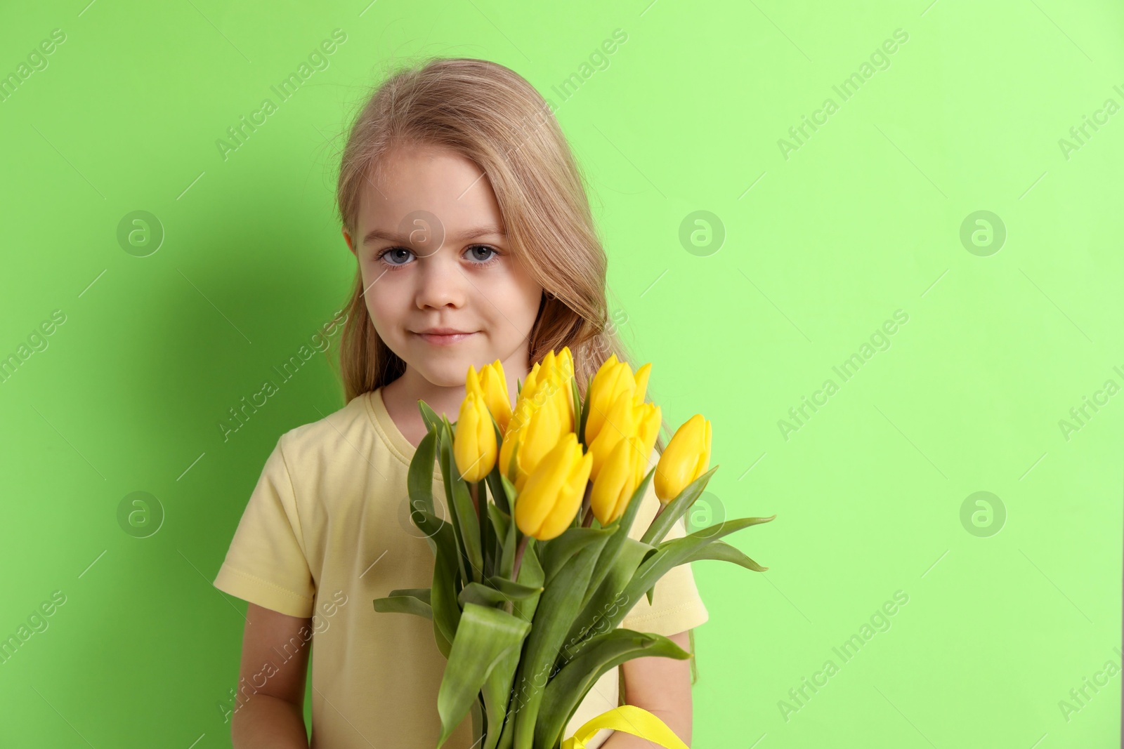 Photo of Cute little girl with beautiful yellow tulips on green background, space for text. Spring season