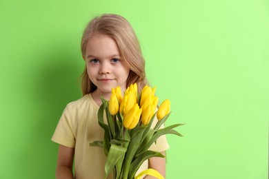 Photo of Cute little girl with beautiful yellow tulips on green background, space for text. Spring season