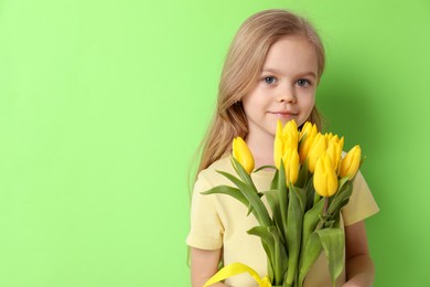 Photo of Cute little girl with beautiful yellow tulips on green background, space for text. Spring season