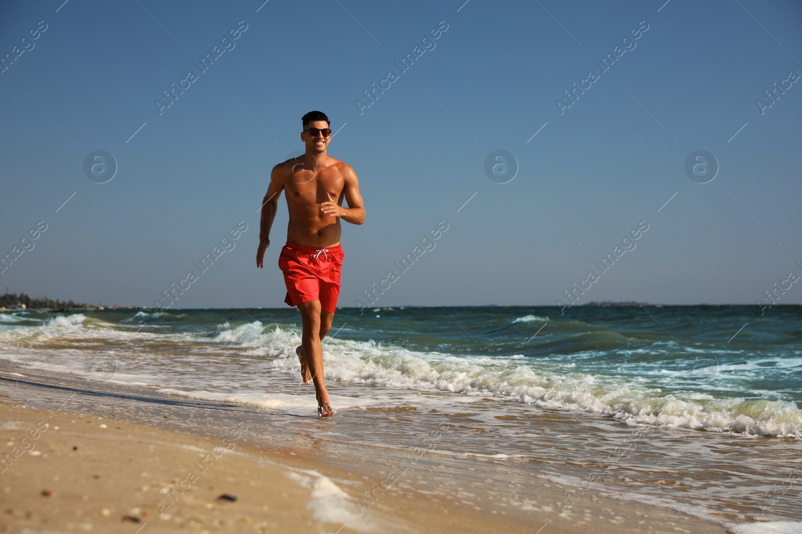 Photo of Handsome man with attractive body running on beach