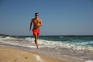 Photo of Handsome man with attractive body running on beach