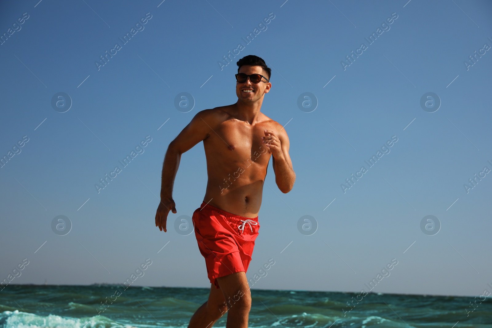 Photo of Handsome man with attractive body running on beach