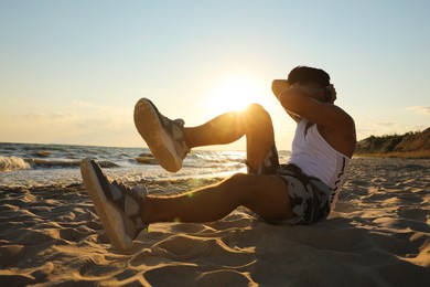 Photo of Sporty man with athletic body doing crunches on beach