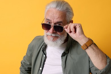 Stylish senior man in sunglasses on orange background