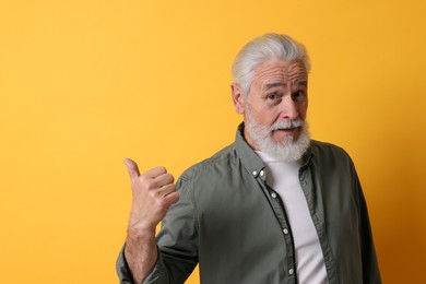 Photo of Senior man pointing at something on orange background. Space for text