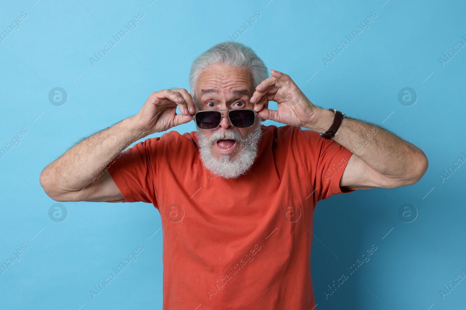 Photo of Emotional senior man in sunglasses on light blue background