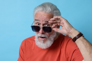 Photo of Emotional senior man in sunglasses on light blue background