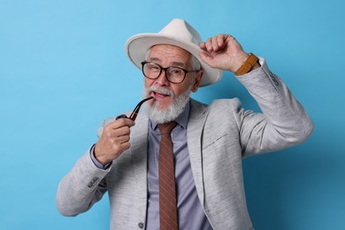 Stylish senior man with tobacco pipe on light blue background