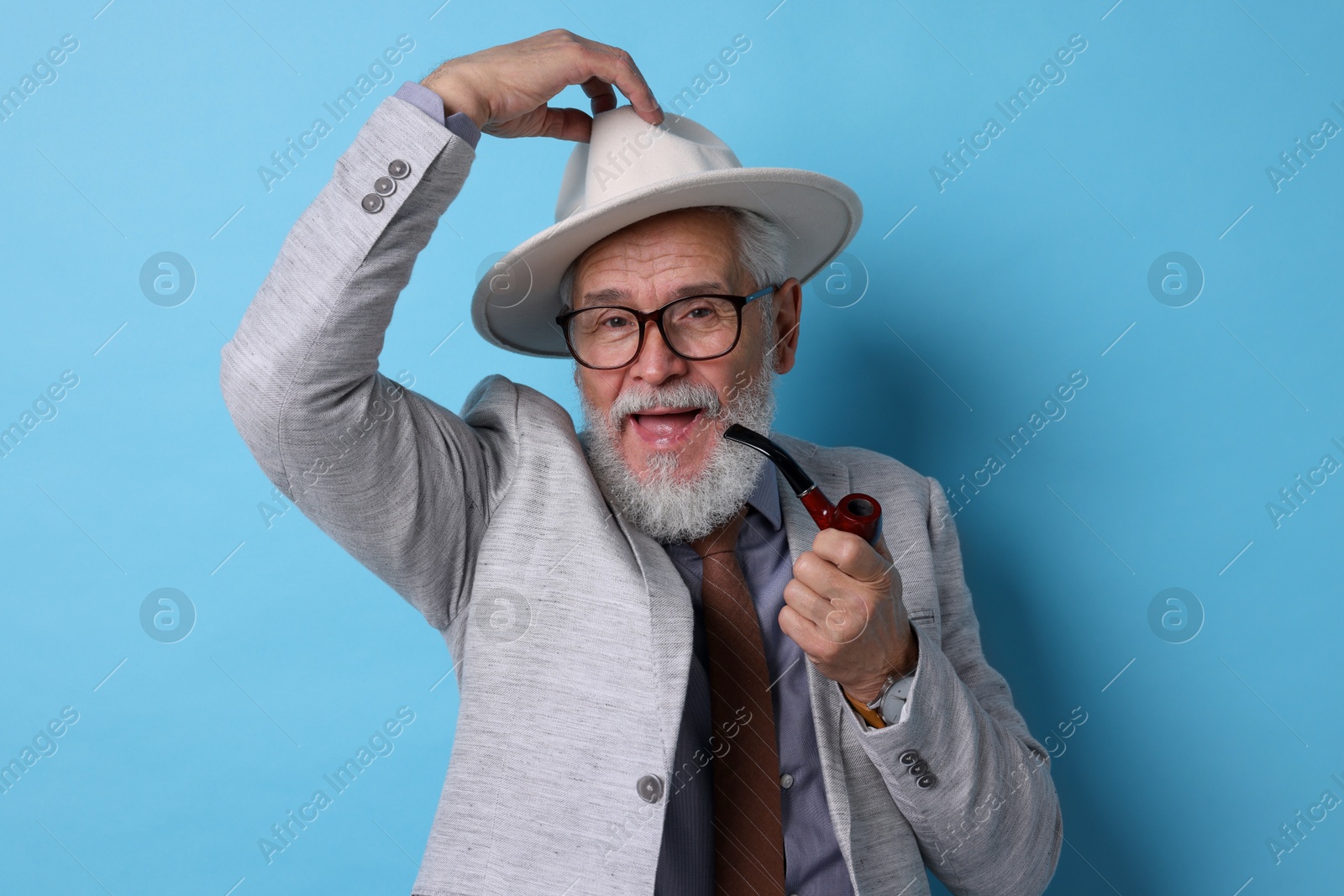 Photo of Stylish senior man with tobacco pipe on light blue background