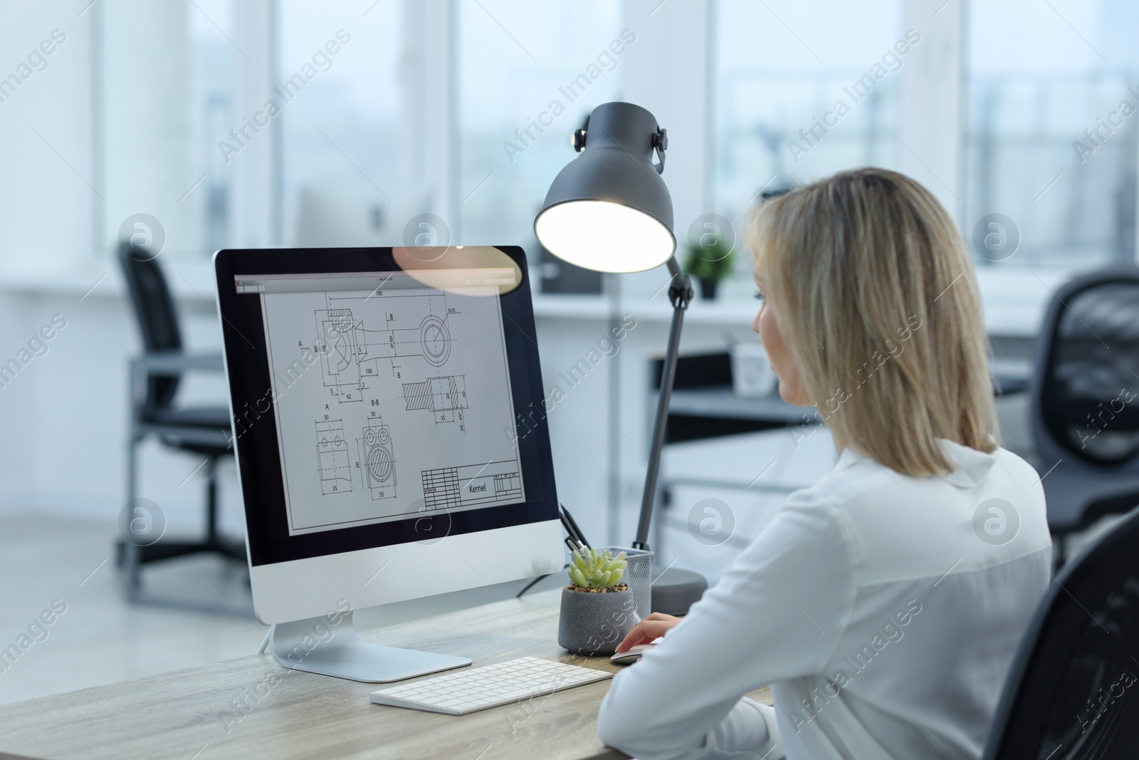 Photo of Technician making digital engineering drawing on computer at desk in office, back view