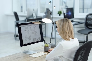 Technician making digital engineering drawing on computer at desk in office, back view