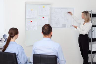 Photo of Woman making presentation with engineering drawings to her colleagues in office