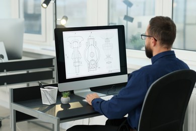 Photo of Technician making digital engineering drawing on computer at desk in office, back view