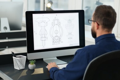 Photo of Technician making digital engineering drawing on computer at desk in office, back view