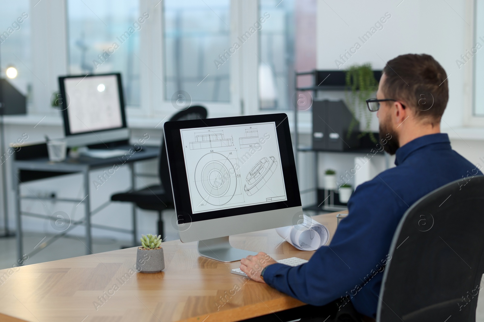 Photo of Technician making digital engineering drawing on computer at desk in office, back view