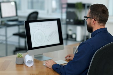 Photo of Technician making digital engineering drawing on computer at desk in office, back view