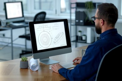 Photo of Technician making digital engineering drawing on computer at desk in office, back view