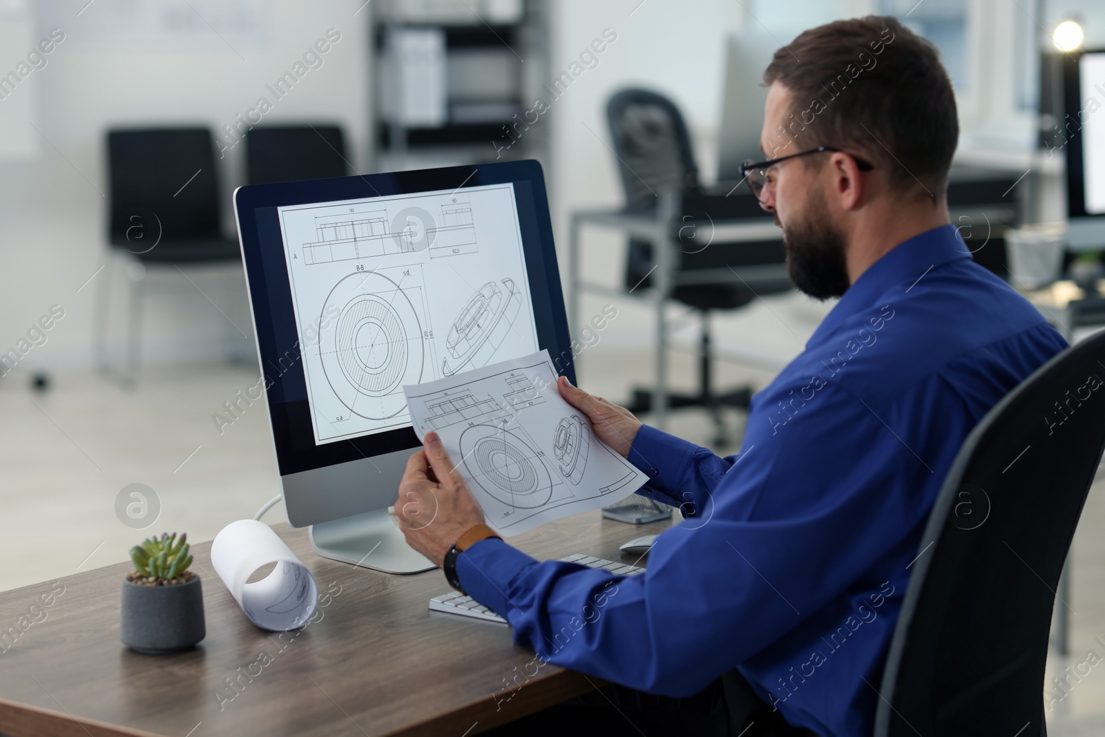 Photo of Technician making digital engineering drawing on computer at desk in office, back view