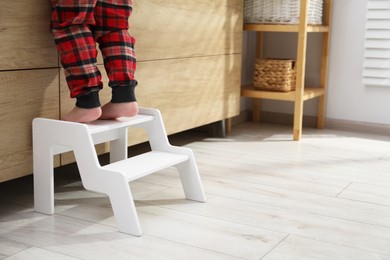 Photo of Little boy standing on step stool indoors, closeup