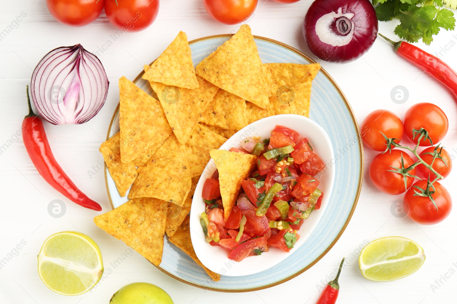 Photo of Delicious salsa (Pico de gallo) served with nachos among products on white wooden table, flat lay