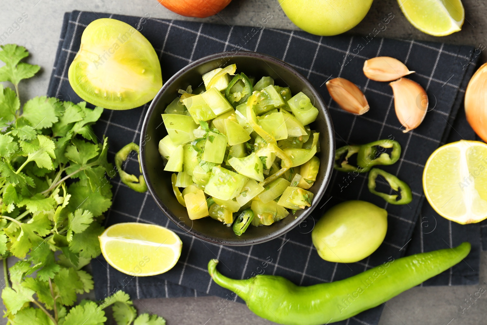 Photo of Delicious salsa (Pico de gallo) in bowl and products on grey textured table, flat lay