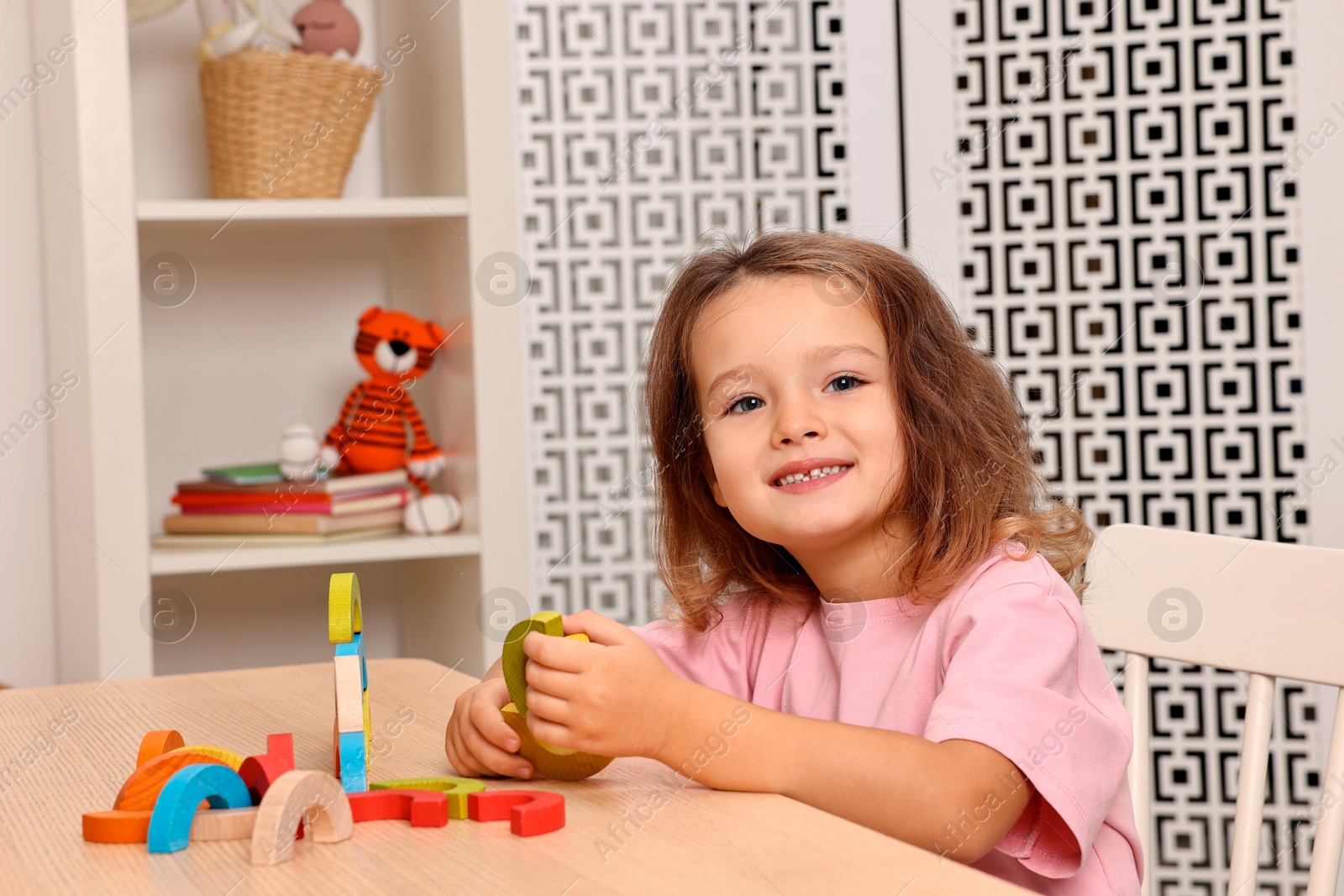 Photo of Autism therapy. Smiling little girl playing with educational toy at table in mental health center