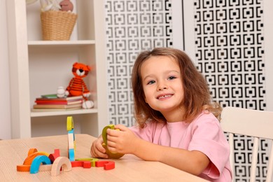 Photo of Autism therapy. Smiling little girl playing with educational toy at table in mental health center